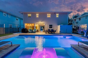 A swimming pool with a slide, a covered patio area, and a house in the background. - Sunni Kai (Fort Myers Beach)