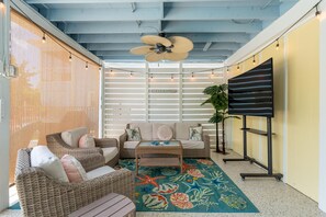 A sunlit room with wicker furniture, a ceiling fan, a TV on a stand, and a decorative rug. - Sunni Kai (Fort Myers Beach)