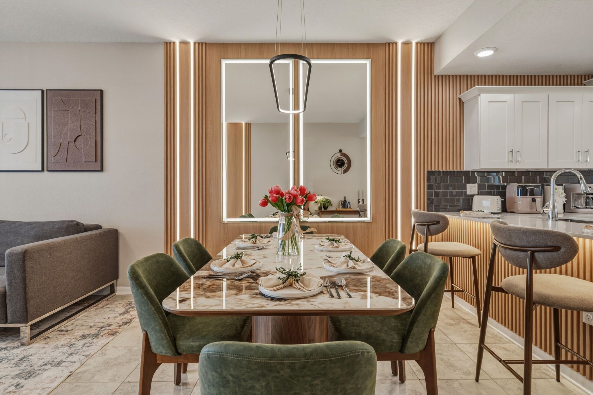Un comedor moderno con una mesa rectangular, sillas tapizadas en verde y un jarrón con flores rojas.