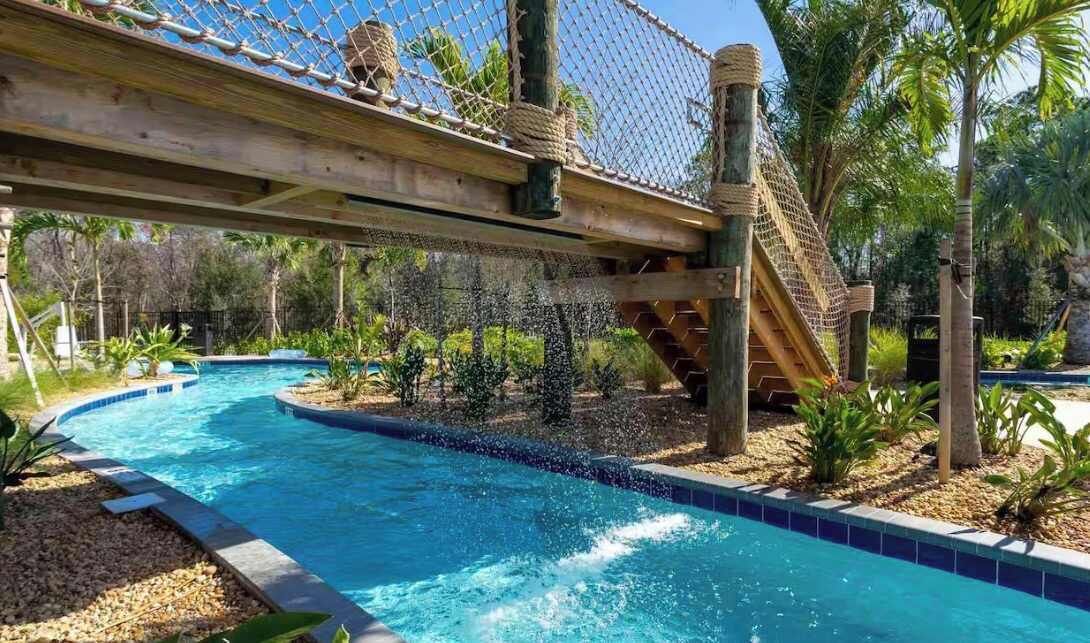 Une piscine avec un pont de corde et des palmiers.