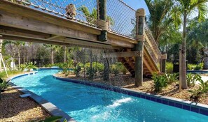 Una piscina con un puente colgante y palmeras.