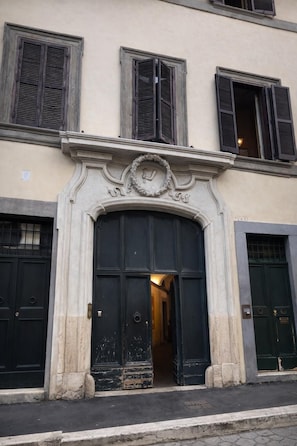 A building facade with a central entrance, flanked by two windows with shutters, and a decorative archway above the doors. - Veronica Suite - Luxury Historic Apartment w/Terrace (Roma)