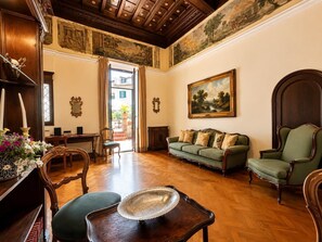 A room with a wooden floor, a green sofa, a wooden chair, a table with a tray, and a painting on the wall. - Veronica Suite - Luxury Historic Apartment w/Terrace (Roma)