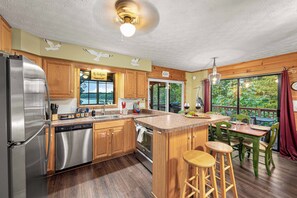A kitchen with wooden cabinets, stainless steel appliances, and a large island with stools. - Lakefront · Dock · 8 Acres · Hot Tub · 2 Fire Pits (Sevierville)