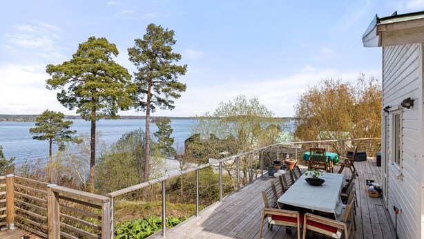 A wooden deck with a table and chairs, overlooking a body of water and trees.