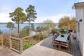 Eine Holzterrasse mit Tisch und Stühlen, mit Blick auf ein Gewässer und Bäume.