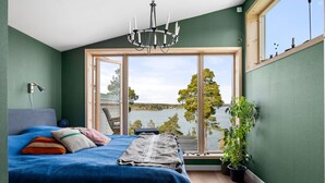 A bedroom with a large window, a bed, a chandelier, and a view of a lake.