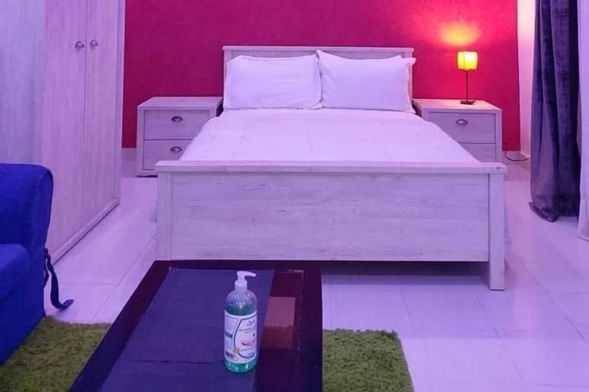 Un dormitorio con cama, mesitas de noche, ventilador de techo y una mesita con lámpara.
