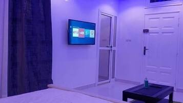 Un dormitorio con una cama, un televisor montado en la pared, una puerta y una mesita.