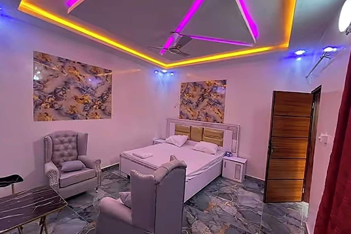 Un dormitorio con cama, una silla, mesita de noche, ventilador de techo y obras de arte en las paredes.