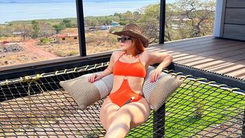 Una persona descansando en una hamaca con vistas a un cuerpo de agua y montañas distantes.
