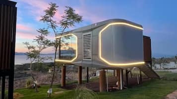 A modern building with a unique design, featuring a curved structure and illuminated edges, situated on a grassy area with a stone pathway.