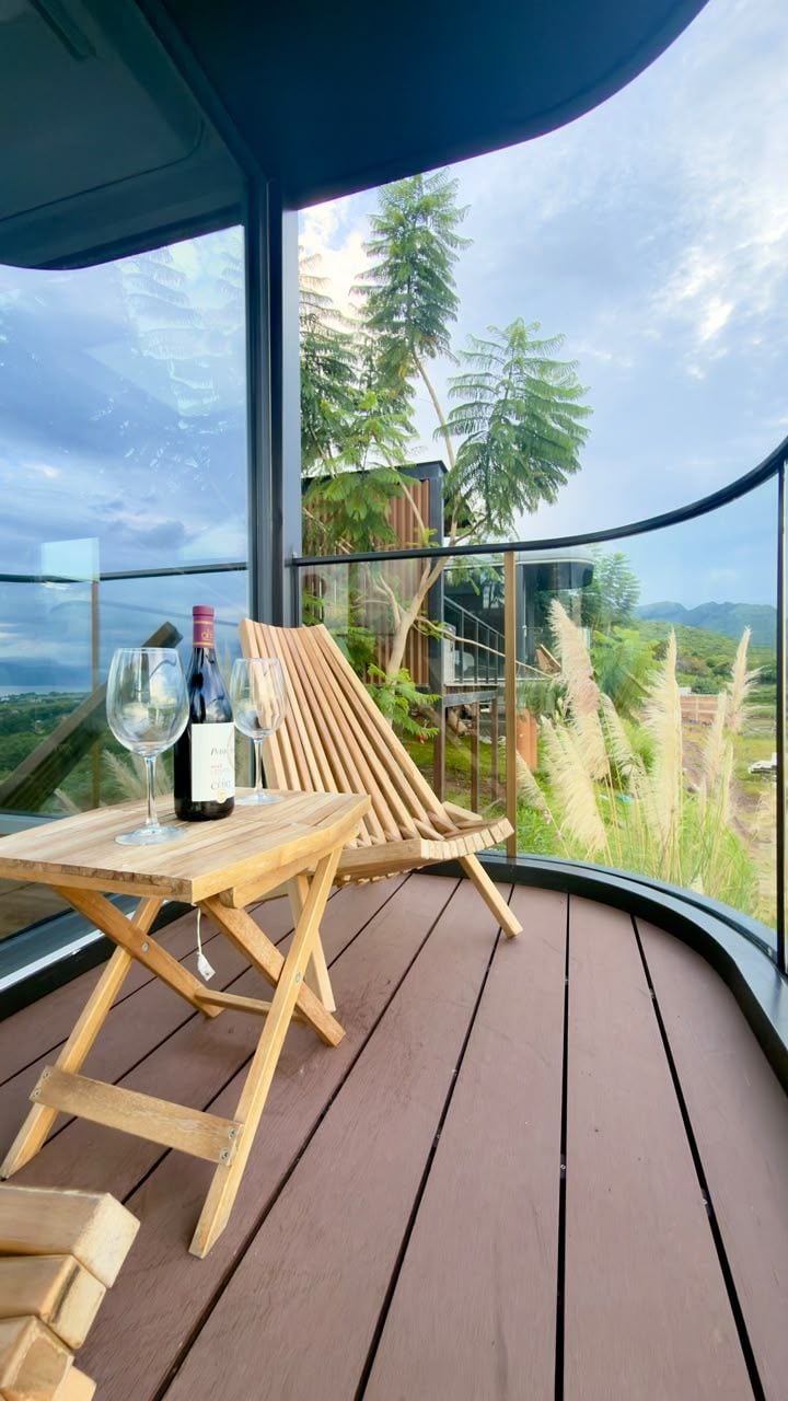 Una terraza de madera con una mesa de vidrio, dos sillas y una botella de vino.