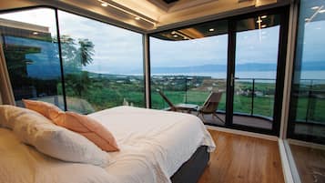A bedroom with a large bed, a view of the outdoors, and a balcony with chairs.