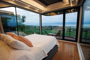 Une chambre avec un grand lit, une vue sur l’extérieur et un balcon avec des chaises.