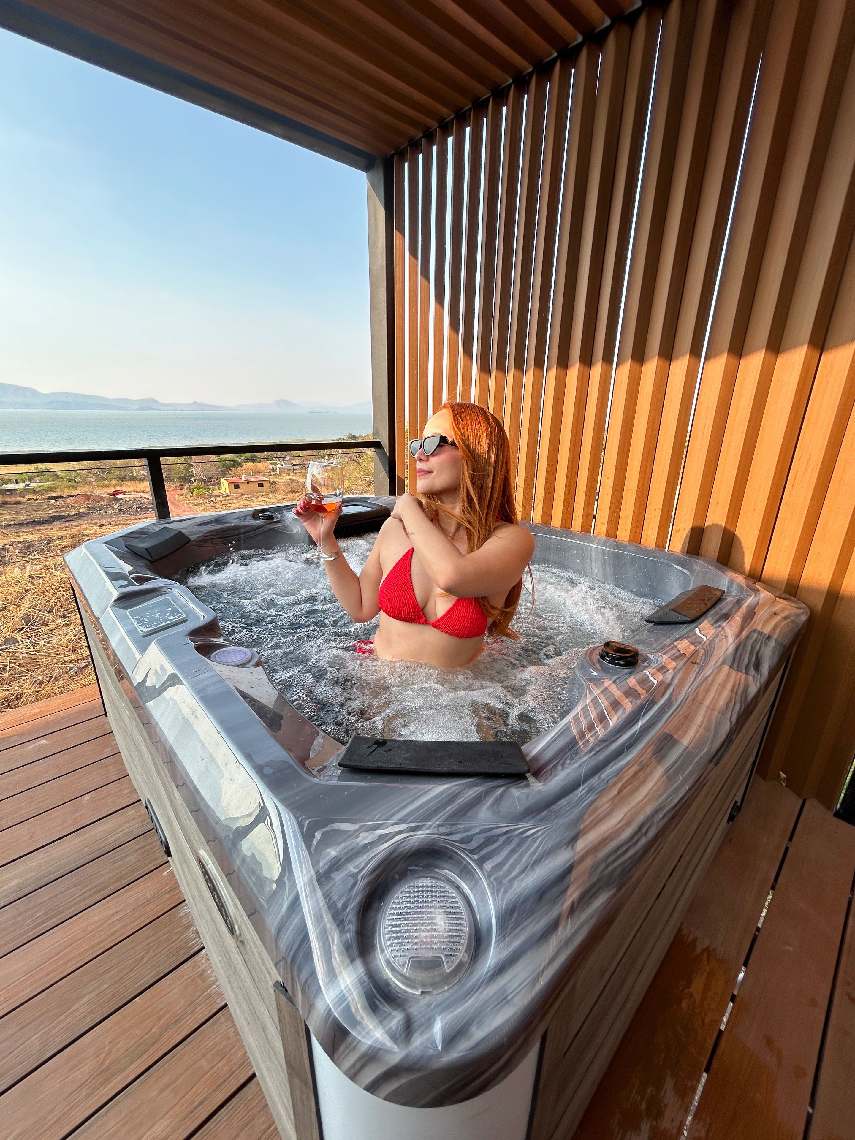 Una persona en un jacuzzi con vista a un cuerpo de agua y montañas.