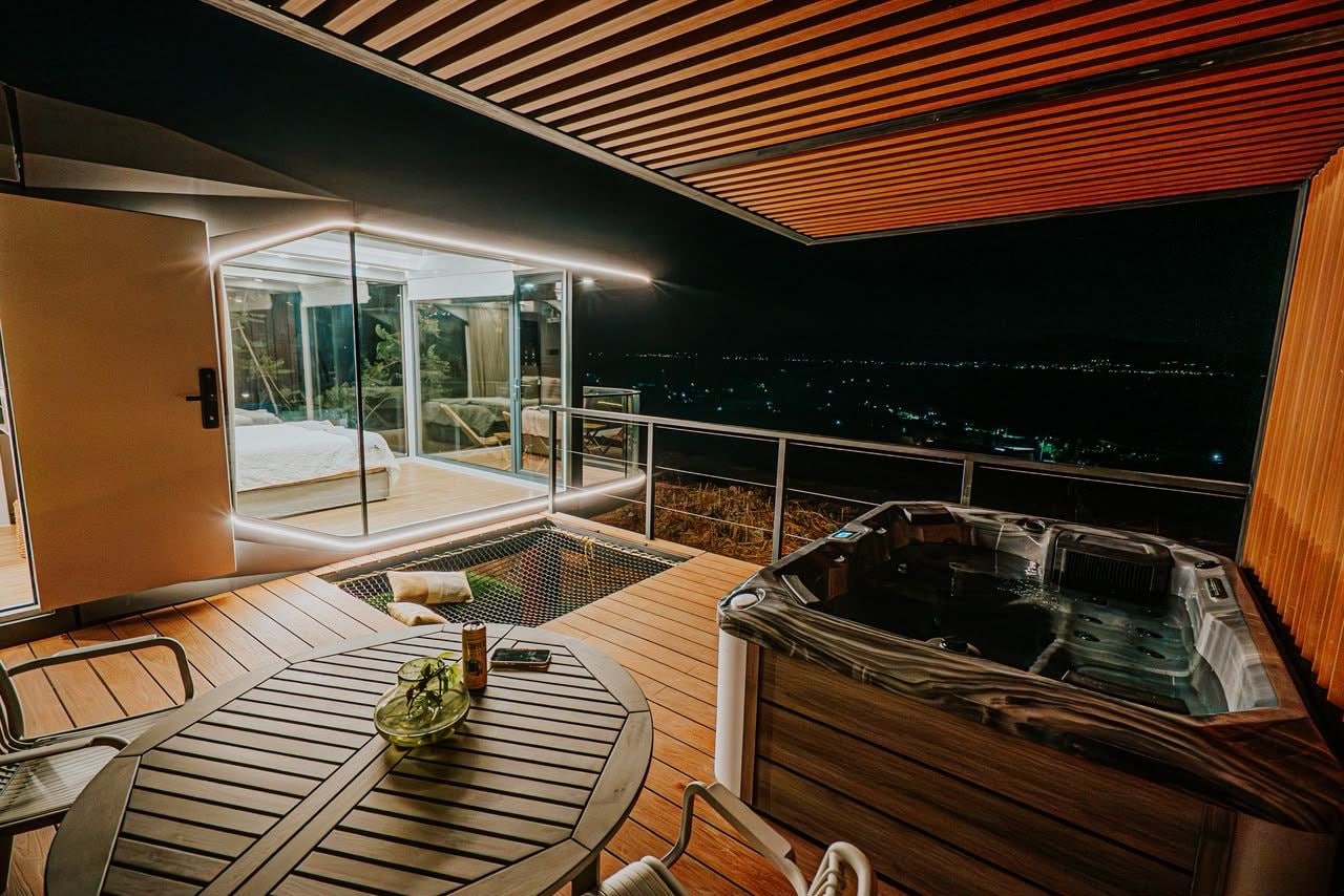 Una terraza moderna al aire libre con un jacuzzi, una sala con paredes de vidrio y vistas a la ciudad de noche.