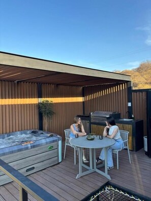 Un patio exterior con un jacuzzi, una parrilla y una mesa redonda con sillas.