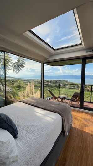 A bedroom with a large bed, a skylight, and a balcony with a view of the landscape.