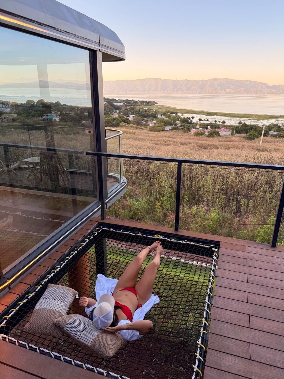 A person relaxing in a hammock on a balcony with a view of a body of water and distant mountains.