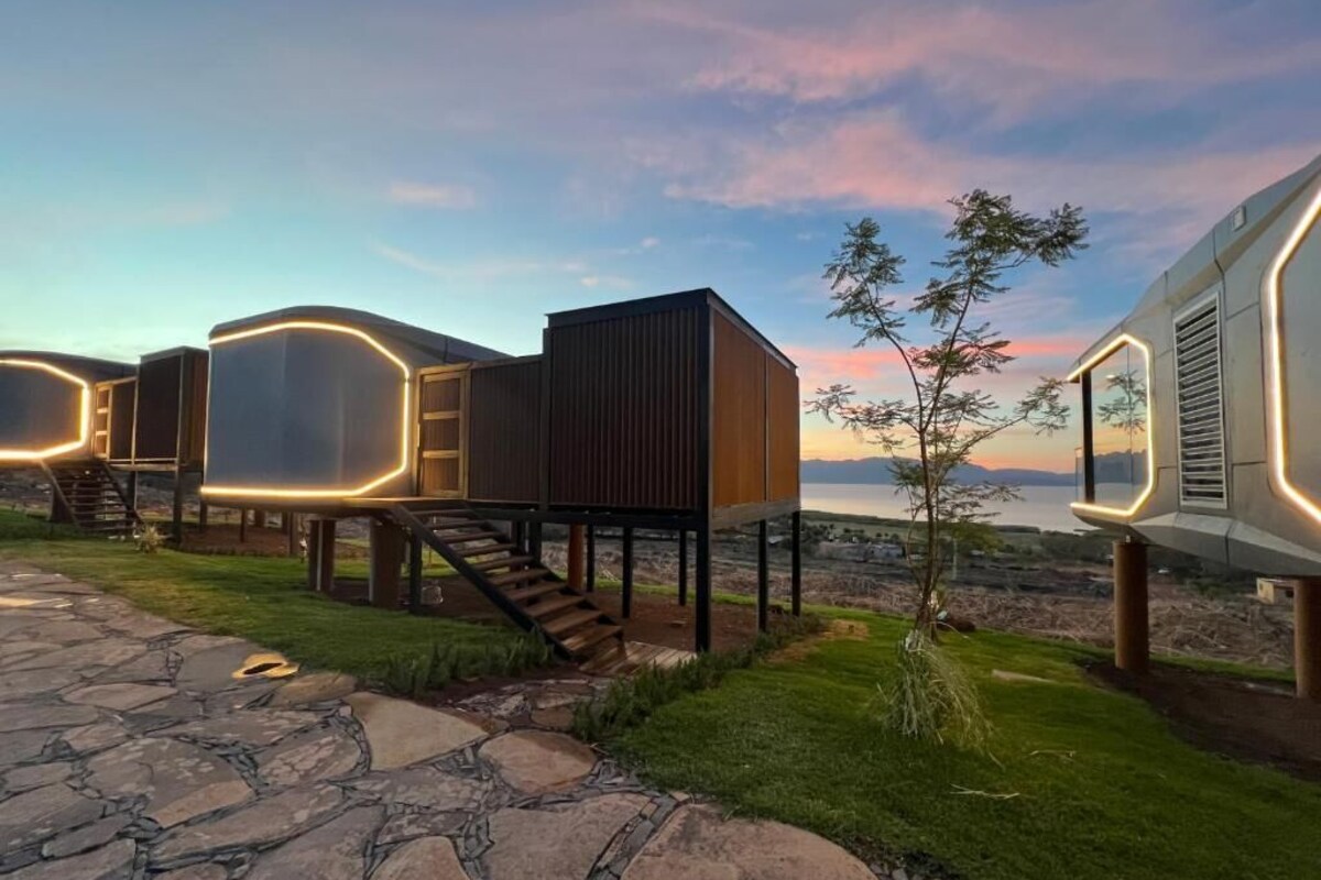 Un edificio moderno con una escalera que lleva a una terraza, rodeado de senderos de piedra y vegetación.
