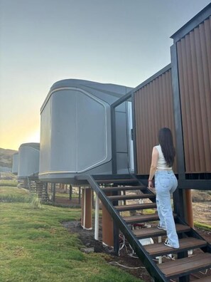 Una persona subiendo una escalera de madera hacia un edificio moderno de techo curvo.