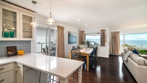 A modern kitchen with a dining area, a sofa, and a view of the sea. - Beachfront · sunrise ocean views, 3BR, BBQ (Campbell River)