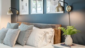 A bedroom with a bed, pillows, a nightstand, a lamp, a framed picture, and a potted plant. - Beachfront · sunrise ocean views, 3BR, BBQ (Campbell River)