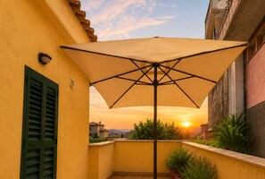 Ein Balkon mit einer großen Sonnenschirm, einem grünen Rollo und einem Blumentopf.