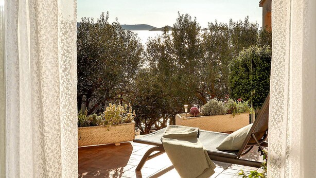 Un espacio de estar al aire libre con vista al mar, rodeado de vegetación y un muro de piedra.