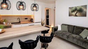 Una cocina moderna con una isla central, taburetes negros, un sofá verde oscuro y un cuadro en la pared.
