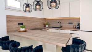 Una cocina moderna con encimera de madera, sillas negras, un lavamanos y luces colgantes.