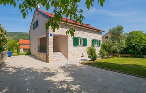 Ein Haus aus Stein mit rotem Dach, grünen Fensterläden und einem gepflasterten Eingang.