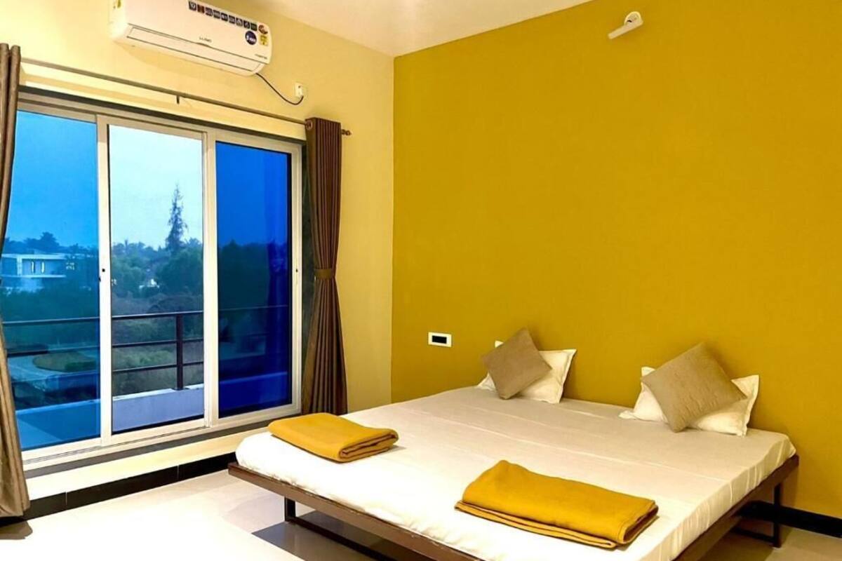 A hotel room with a bed, a window, curtains, and an air conditioning unit.