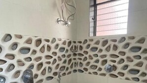 A bathroom with a unique stone-patterned wall, a toilet, a shower, and a hand dryer. - Scarlet Stays (Alibag)
