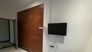 A room with a brick wall, a flat-screen TV mounted on the wall, and a bench. - Scarlet Stays (Alibag)