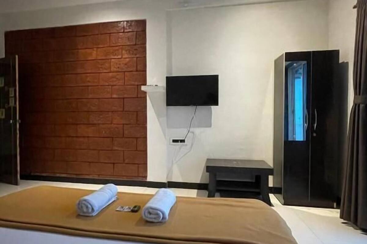 A hotel room with a bed, a television mounted on the wall, a wooden accent wall, and a ceiling fan.