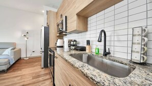 A modern kitchen with a granite countertop, stainless steel sink, wooden cabinets, and white subway tiles.