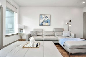 A modern living room with a sectional sofa, a small side table, a Buddha statue, and a painting on the wall. - Luxury Houston Apartment: Rooftop Pool, City Views & King Beds Near Downtown (Houston)