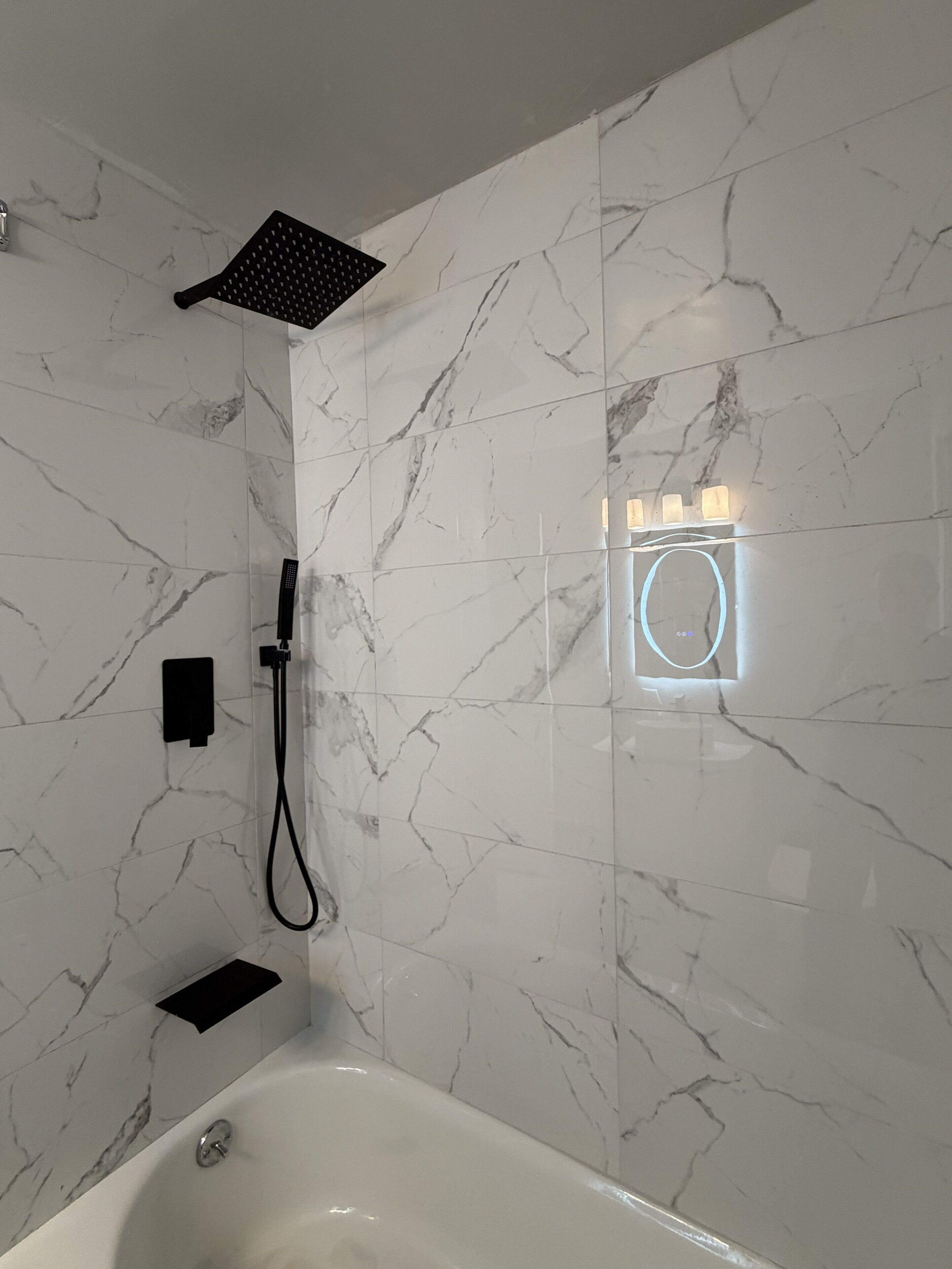 A modern bathroom with a bathtub, a shower head, and a wall-mounted light fixture.