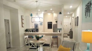 A modern kitchen with a central island, a dining area with a round table and chairs, and a living area with a sofa and a lamp. - Spacious 3BR Resort Condo Near Disney (Davenport)