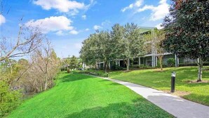 A well-maintained grassy area with a pathway leading to a building with multiple windows. - Spacious 3BR Resort Condo Near Disney (Davenport)