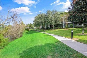 A well-maintained grassy area with a pathway leading to a building with multiple windows. - Spacious 3BR Resort Condo Near Disney (Davenport)