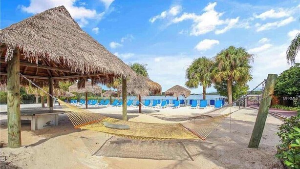 A beach with thatched-roof structures, hammocks, and sun loungers. - Spacious 3BR Resort Condo Near Disney (Davenport)
