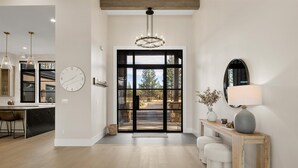 A modern interior with a kitchen, a wooden bench, a lamp, and a large window with a view. - Brand-New Lakefront Estate | Private Lake + Hot Tub | Outdoor Living (Bend)