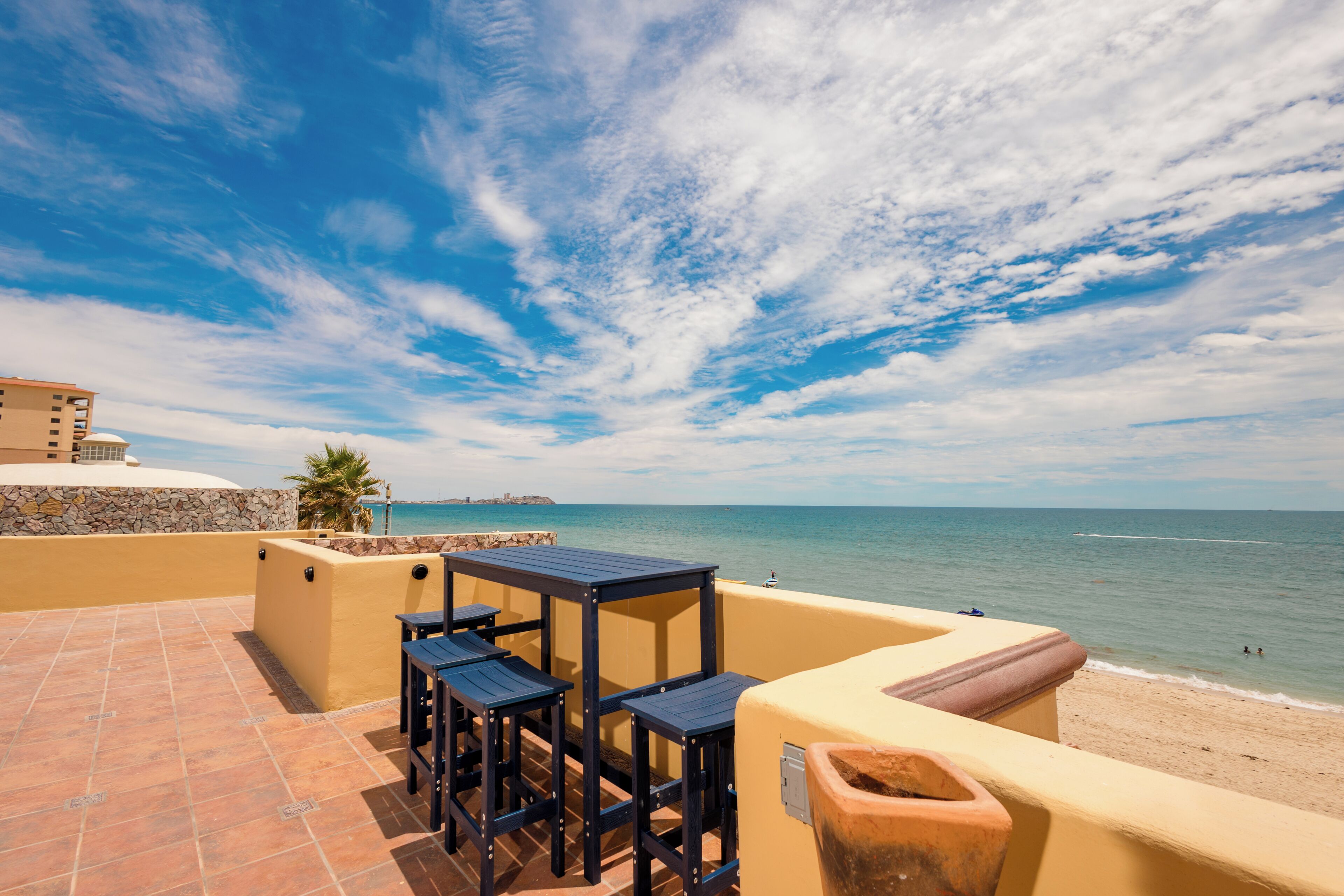 Eine Terrasse mit Tisch und Stühlen mit Blick auf einen Strand und das Meer.