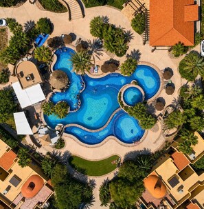 Vista aérea de un complejo turístico con varias piscinas, palmeras y una combinación de edificios residenciales y comerciales.