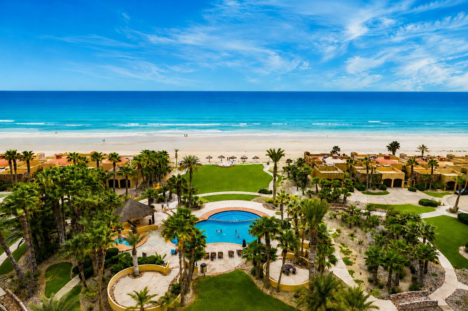 A resort with a swimming pool, palm trees, and a beach view.