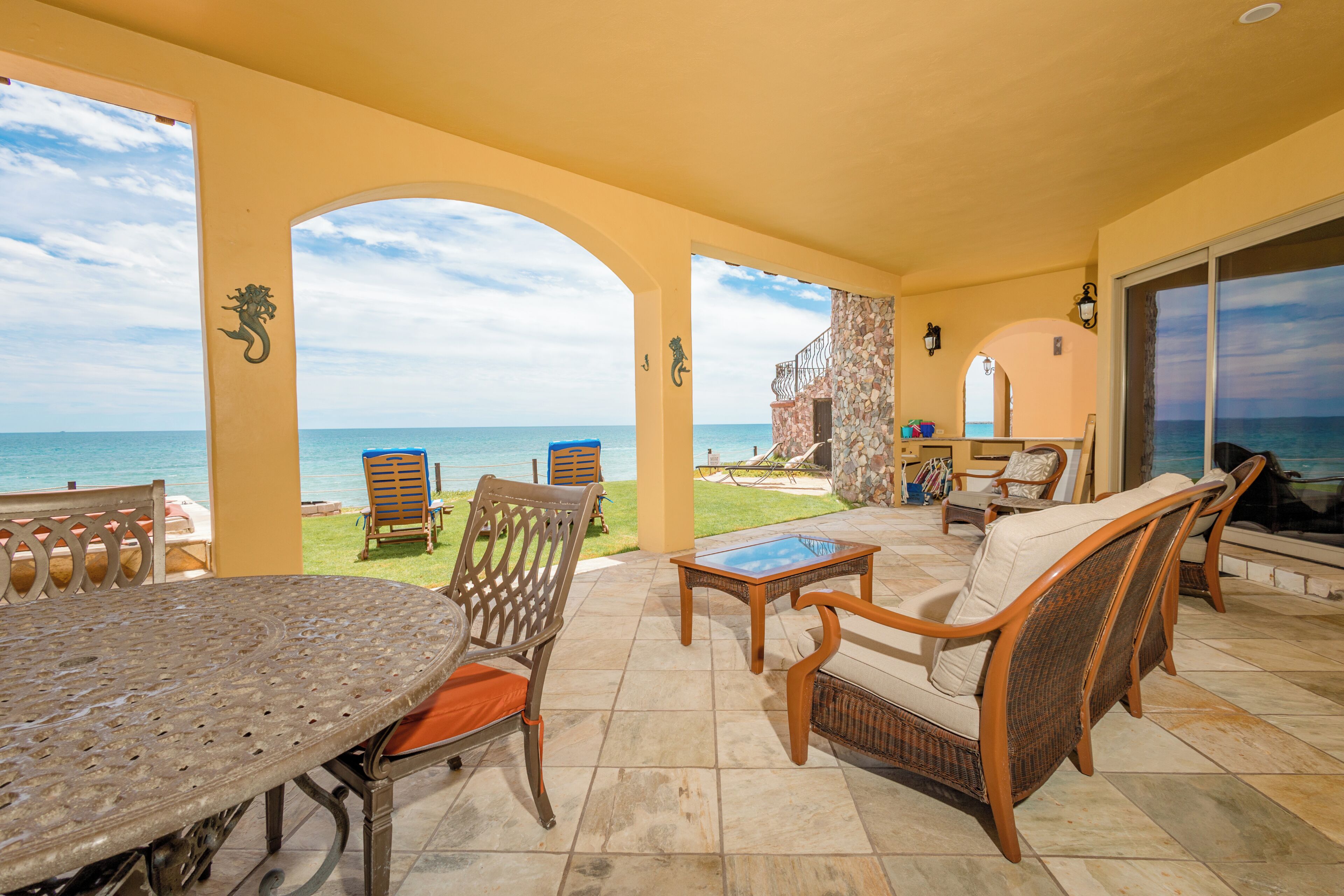 A covered outdoor seating area with a view of the sea, featuring a table, chairs, and a sofa.