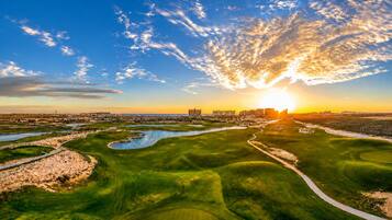 A golf course with a river, a sunset, and buildings in the distance.